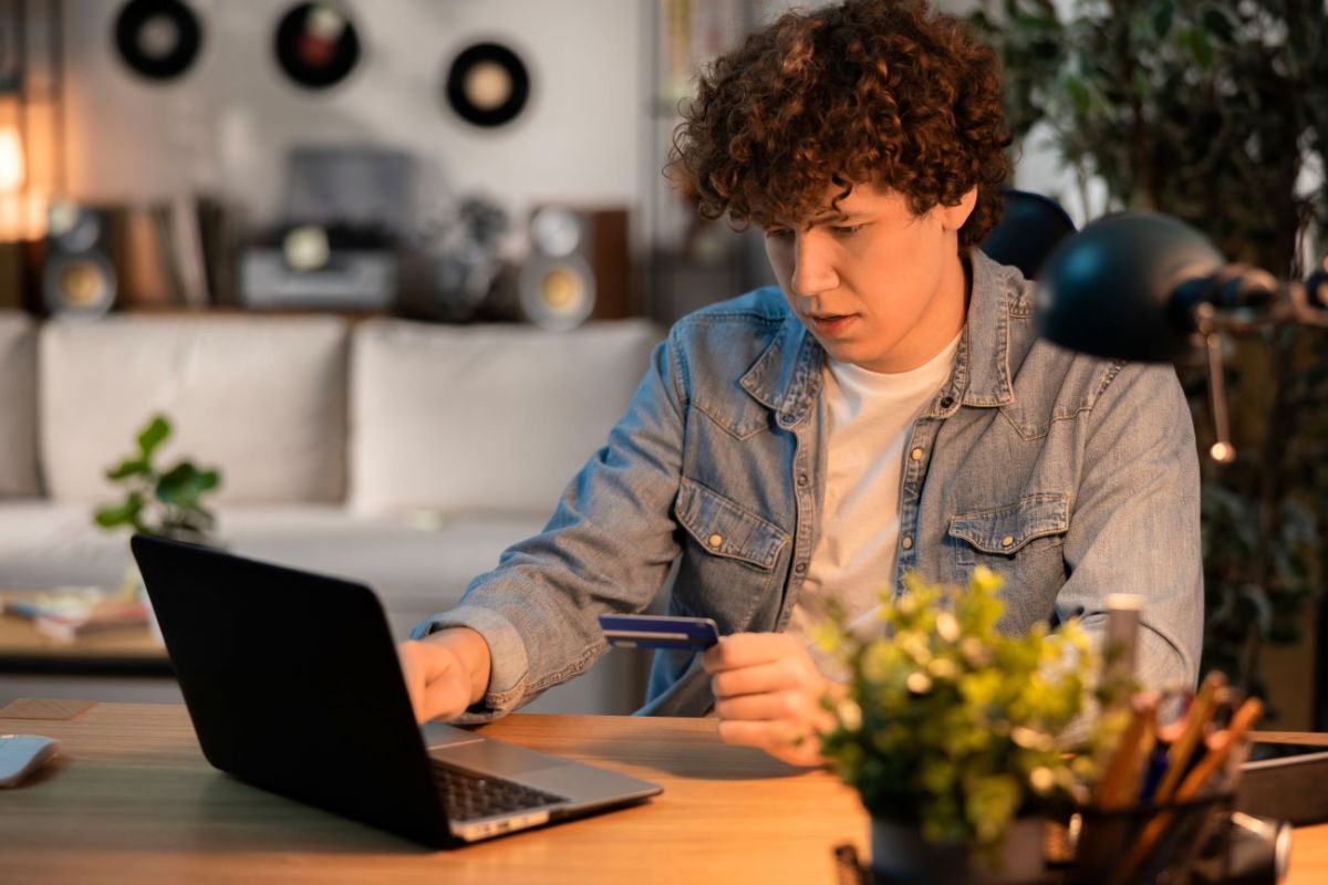 Teen boy holds debit card and makes budget on his laptop
