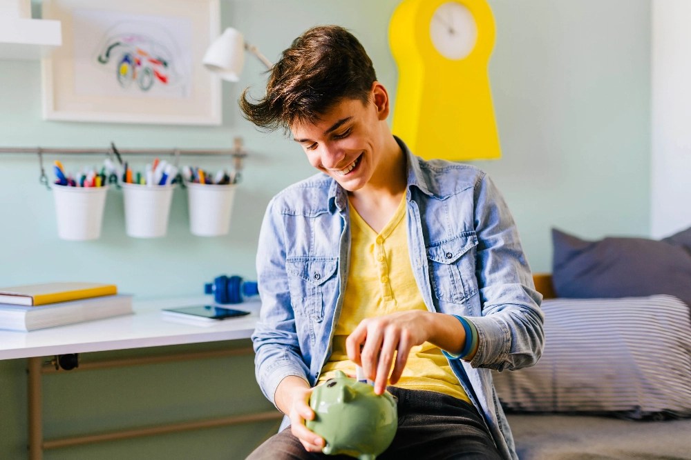 A teen boy putting money in a piggy bank A teen boy putting money in a piggy bank