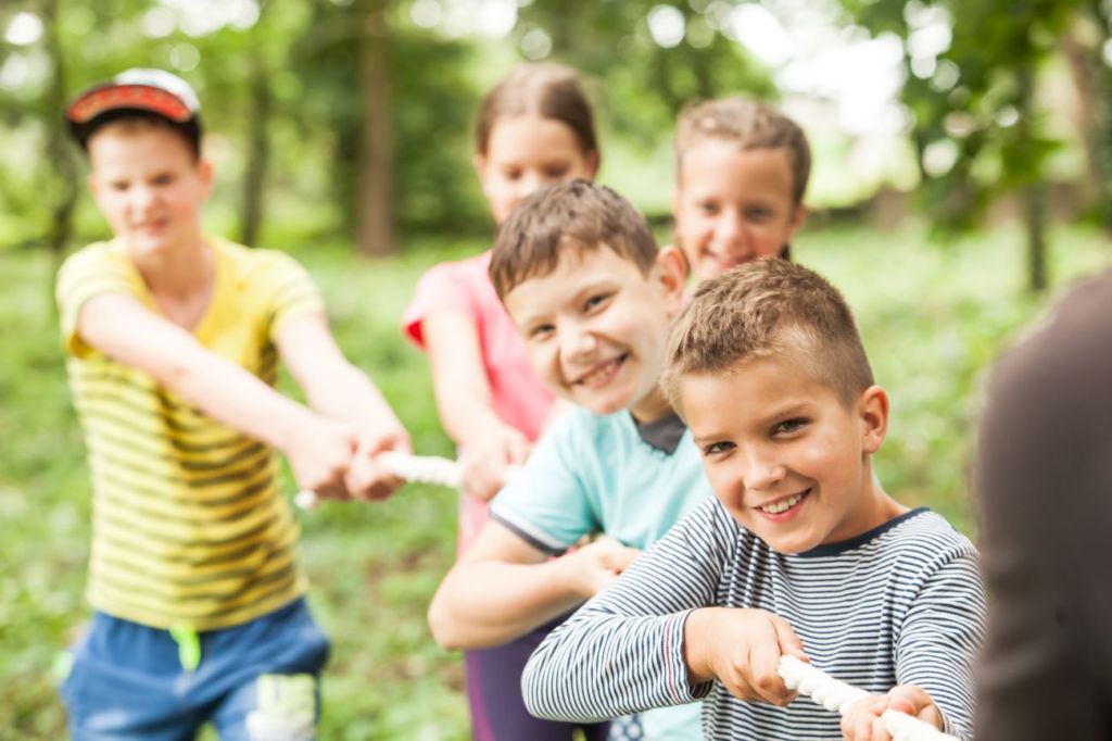 Young children playing tug-of-war at a camp being watched by a part-time teen counsellor