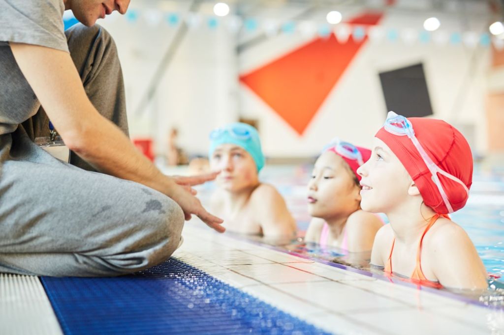 A tween boy working as a swim instructor with younger children