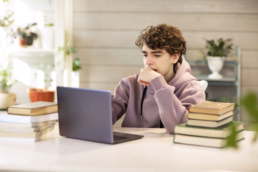 teen boy looks thoughtfully at laptop writing cover letter for job