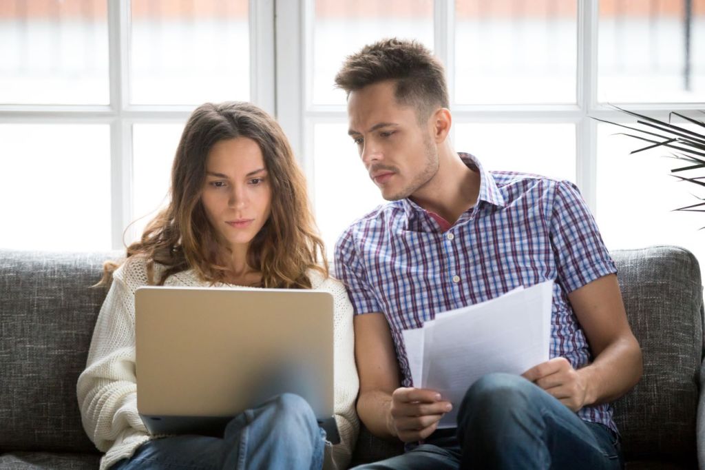 two coparents sit on couch holding papers discussing finances