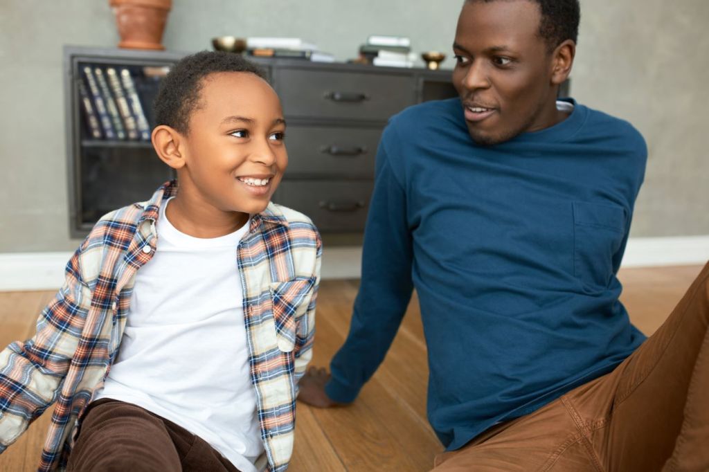 boy and single father sit on floor smiling and talking