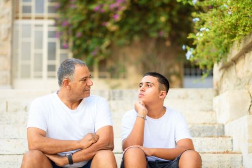 father and son sit on steps discussing finances