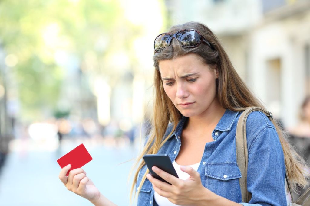 Girl looks at phone, holding cash card, worried about money