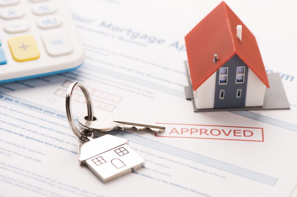 House key, model house, and calculator sit on mortgage paperwork