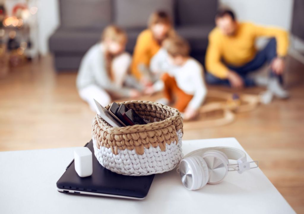 Phones in woven basket as family takes digital detox and plays games in background