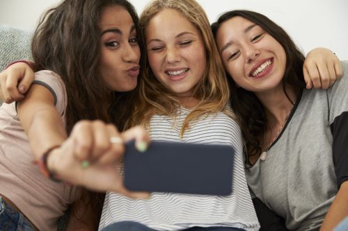 three teenage girls smile and pose holding smart phone screen