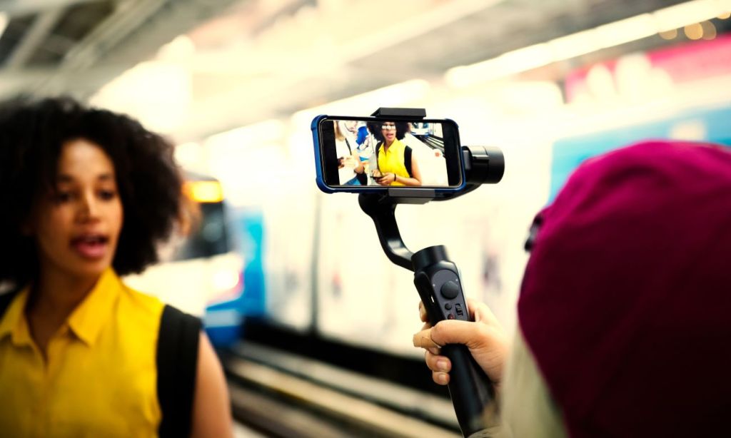 Black woman standing at railway station being filmed for TikTok