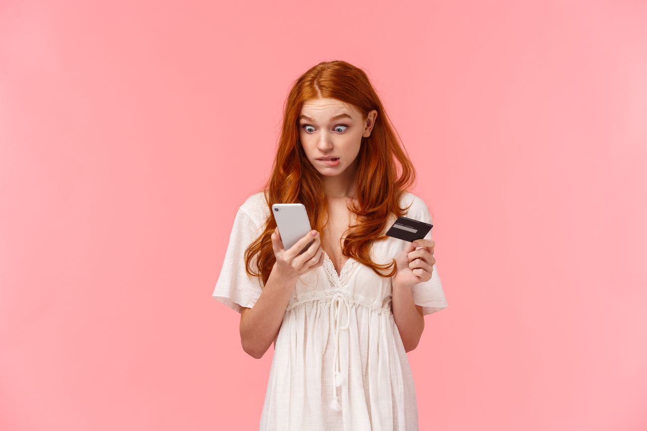 teen girl looking at phone and holding bank card looking concerned