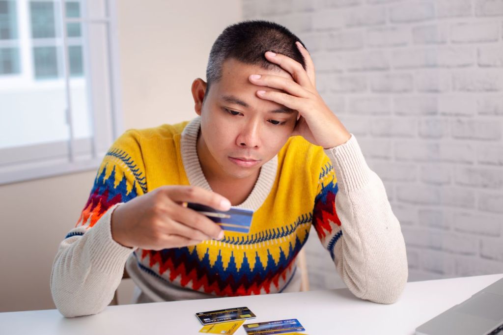 Man with bright coloured sweater looks sad as he stares at credit card