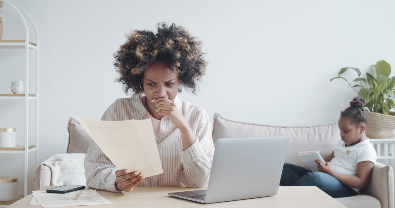 Woman looking at bank statement worried about money with girl sitting on couch