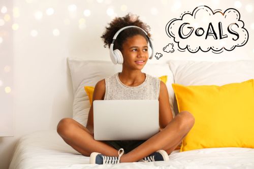 girl wearing headphones sitting on bed with laptop and word "goals" as thought bubble