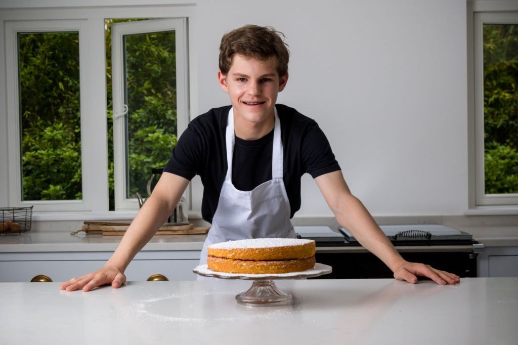Teen boy wearing an apron smiling standing over cake