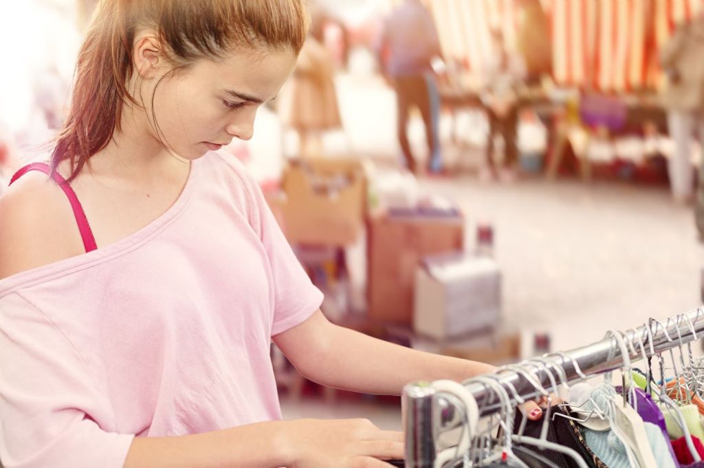 Teen girl going thrifting and looking through rack of clothes