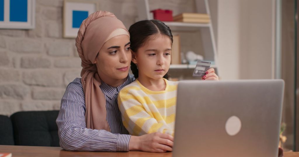 Woman teaching girl financial literacy and looks at computer