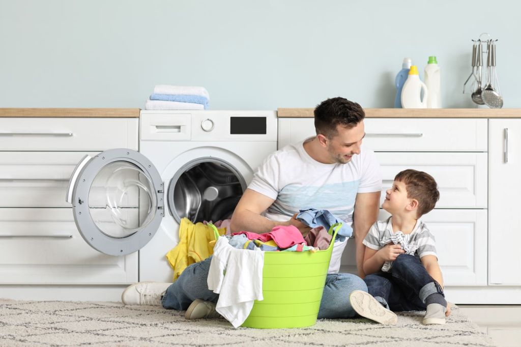 Man and boy sitting on floor in front of laundry machine sorting laundry