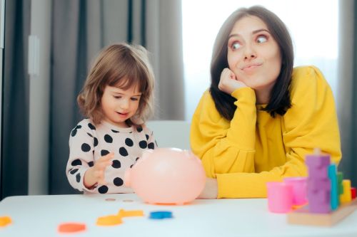 Young girl plays with piggy bank as woman in yellow sweater looks on