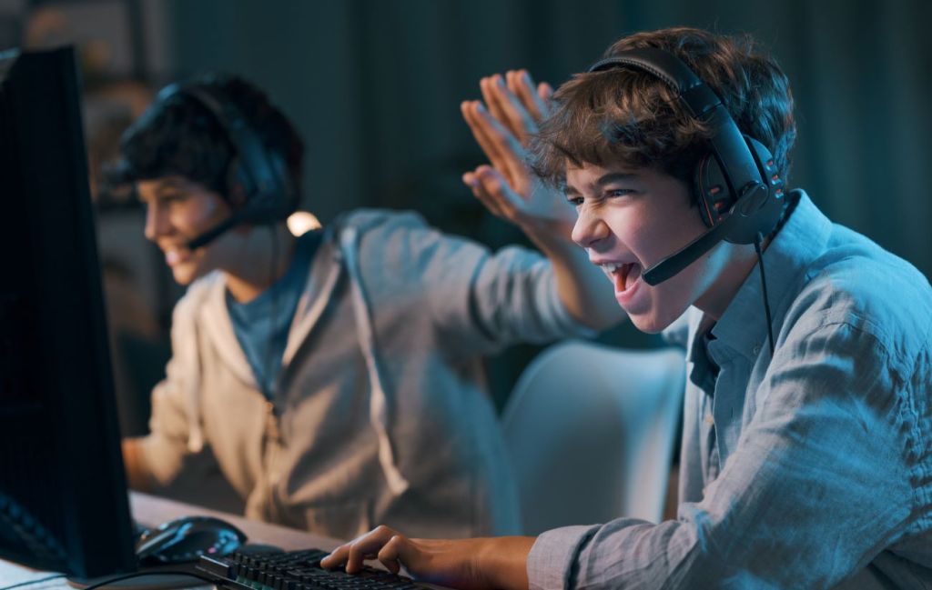 Two teen boys at computer livestreaming their video game and highfiving each other