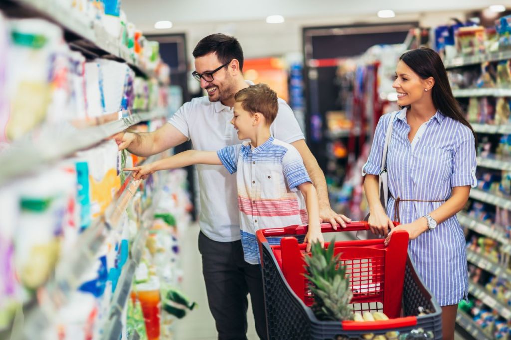 Man, woman, and boy pushing shopping cart and price comparing groceries