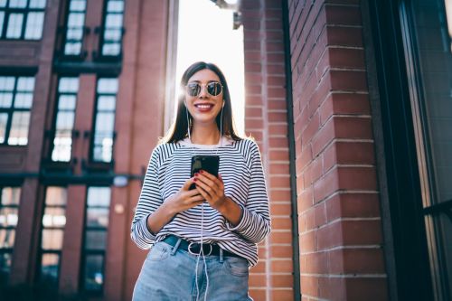 Woman with stripped shirt smiling and walking listening to podcast