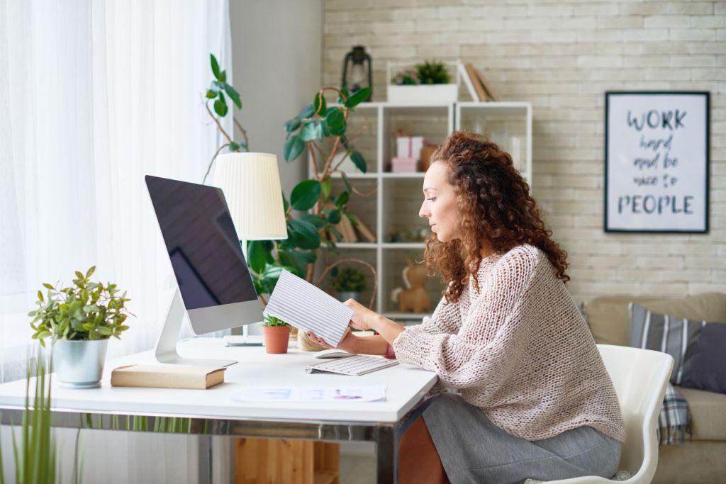 Woman sitting at her home office desk reading papers.