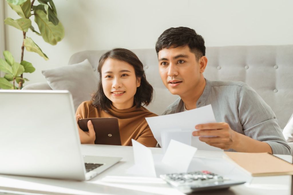 Man and woman sitting on floor in living room looking at computer screen doing taxes