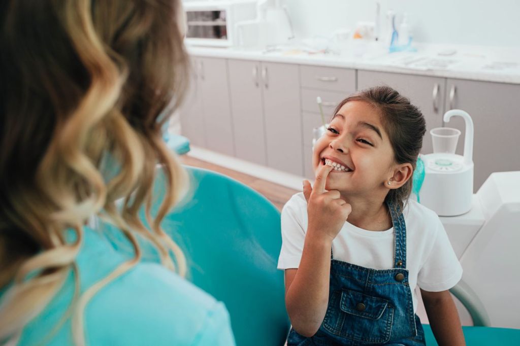 Girl sitting in a dental chair showing her teeth to a dentist