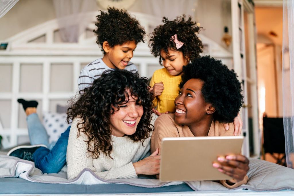 Image of family with two smiling women lying down and two kids sitting on top of them.