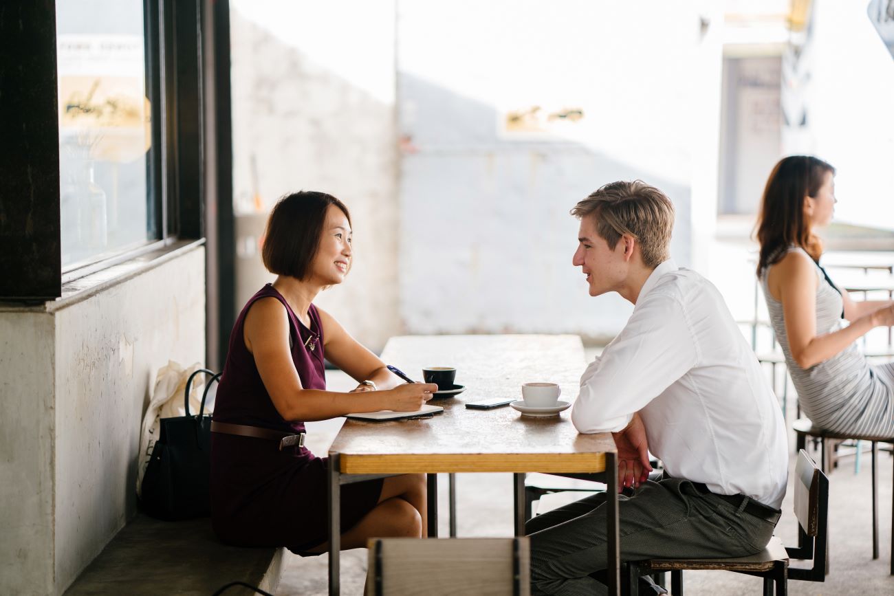 Asian woman sits across from teen boy at coffee table conducting job interview.