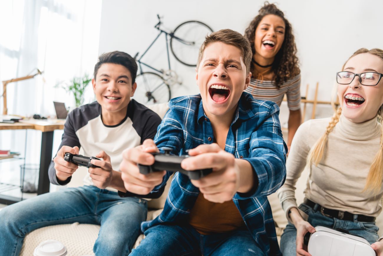 Group of teens, two boys, two girls, laughing, yelling out as they play video games.