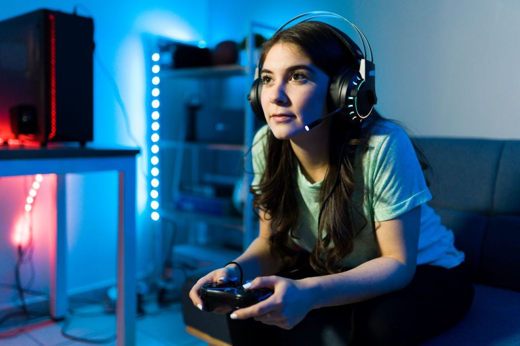 Image of teen girl holding video controller, wearing headphones, staring at screen playing games