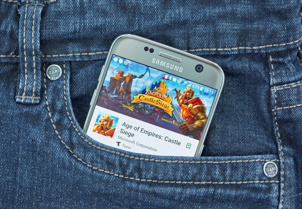 Image of smartphone sticking out of pocket of jeans showing Age of Empire video game on screen.