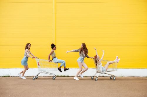group of four teen girls in shopping carts against a yellow brick wall