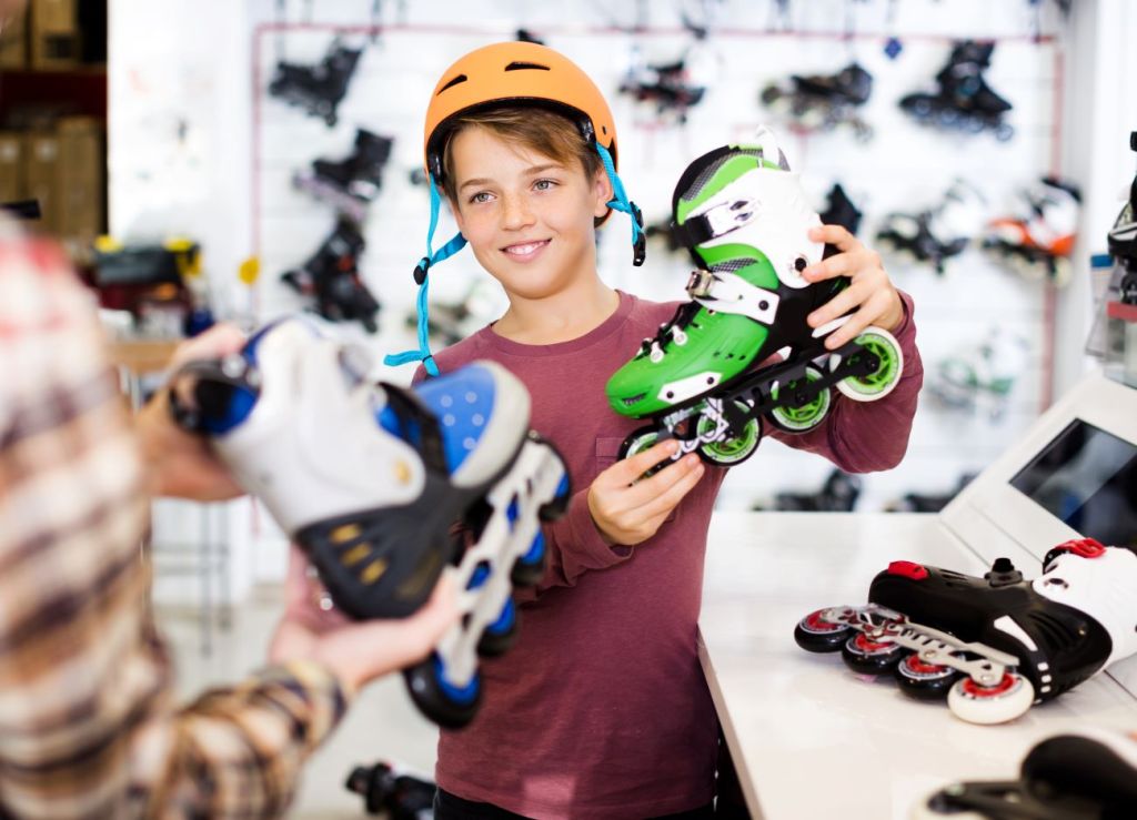 Teen boy wearing orange bike helmet holding up rollerblades and smiling 