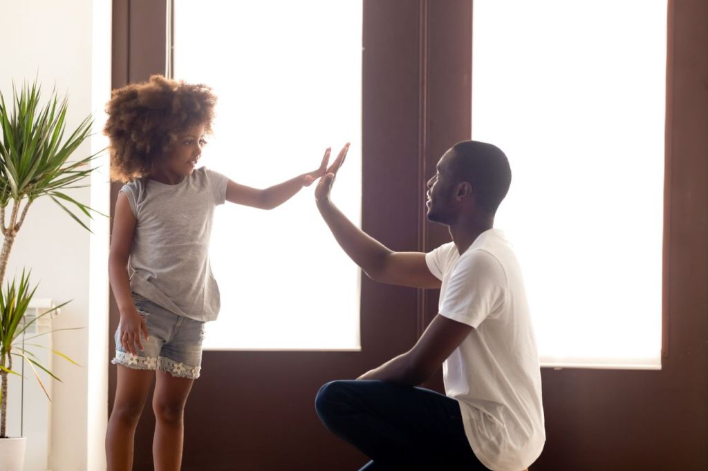 Young Black girl high fives Black man who is kneeling on the floor