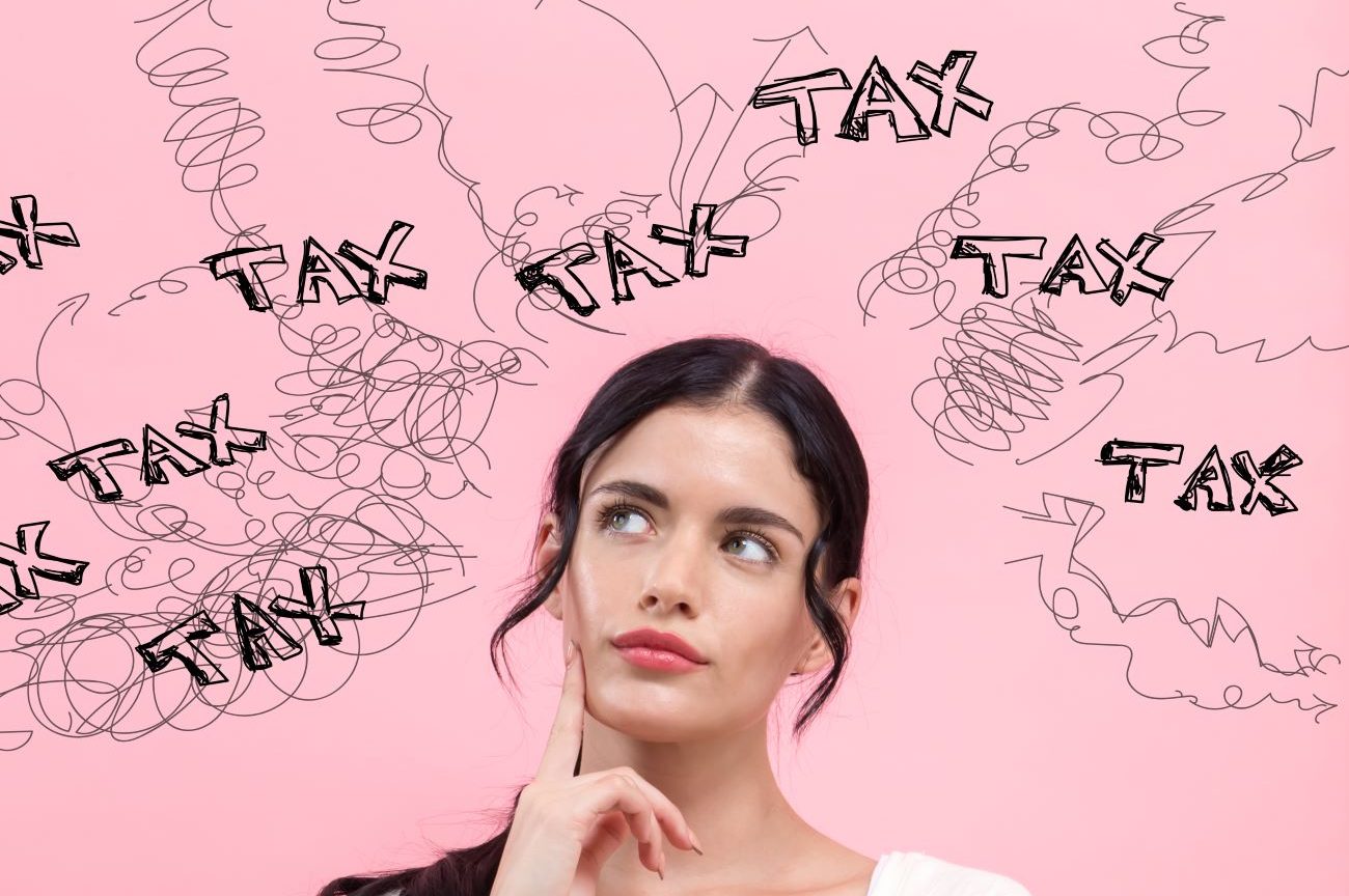 Young woman stands in front of pink background with word "tax" written above her head looking concerned.