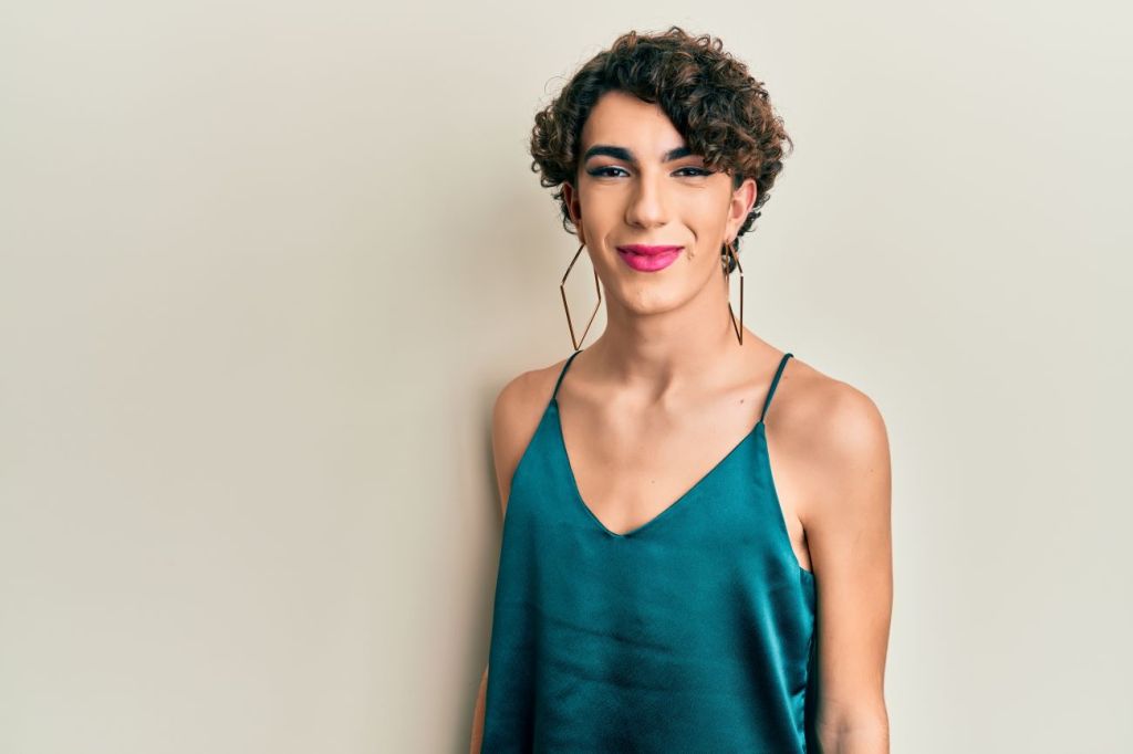 Queer male teen dressed in green top, large earrings, wearing makeup