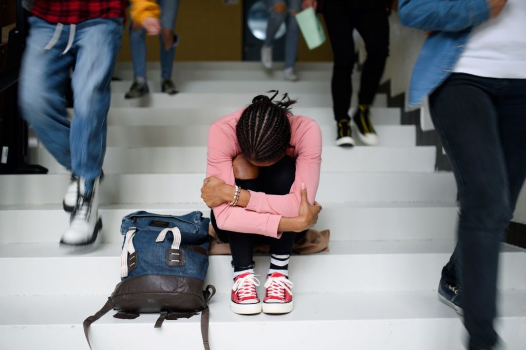 Teen girl sitting on stairs at school with arms folded, head lowered. 