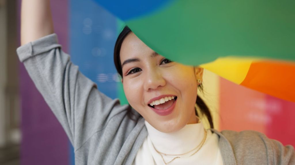 Smiling Asian teen girl holding Pride flag above her head 