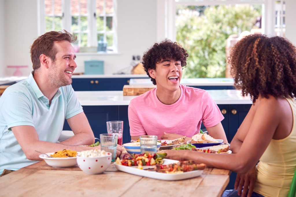 Family With Teenage Son Sitting Around Table At Home Eating Meal Together discussing money