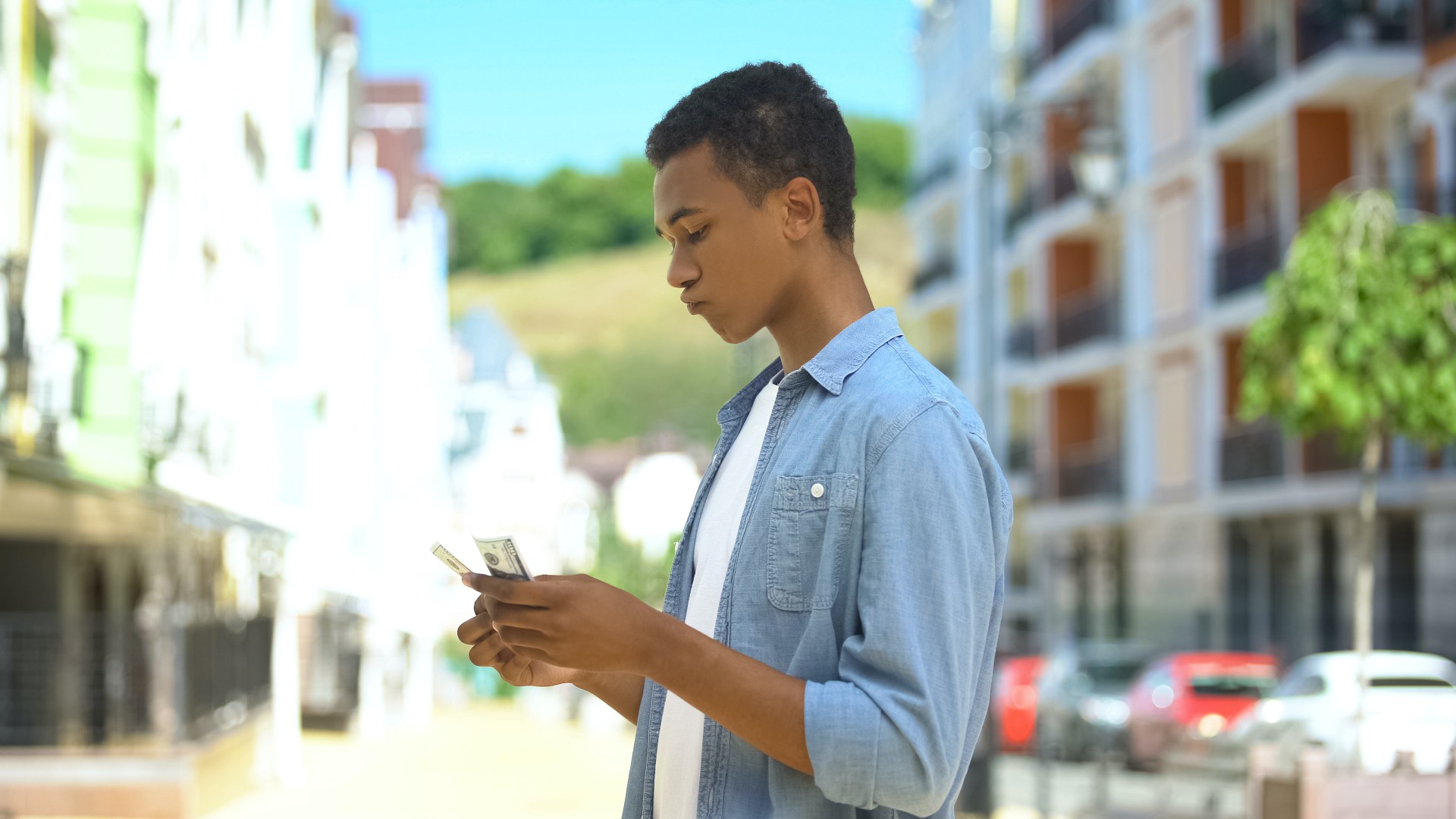 Biracial teen boy counting dollars outside