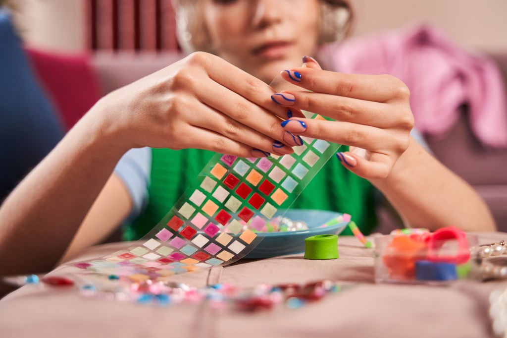 Teen girl making hand made jewellery and listening music while sitting at home