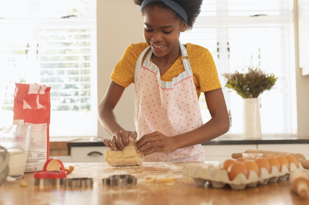 Front view of Black teen girl baking cookies for her own business in kitchen at home