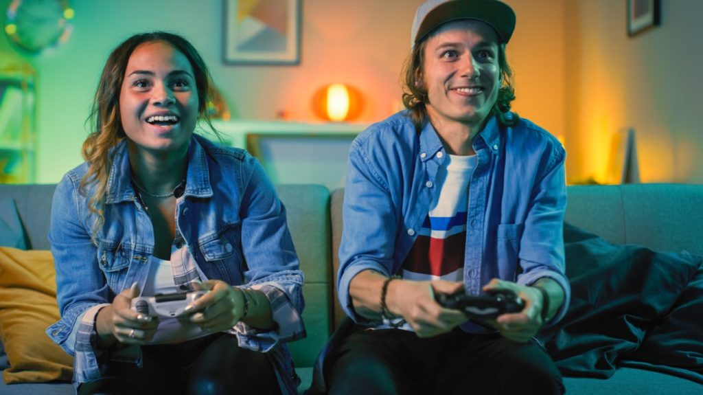 Excited Black teen girl and white teen boy sitting on the couch gaming.