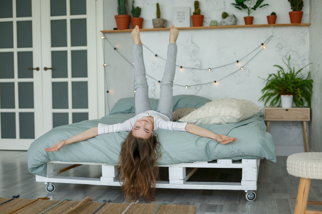 Teen girl lying on pallet bed in her bedroom with string lights in the background