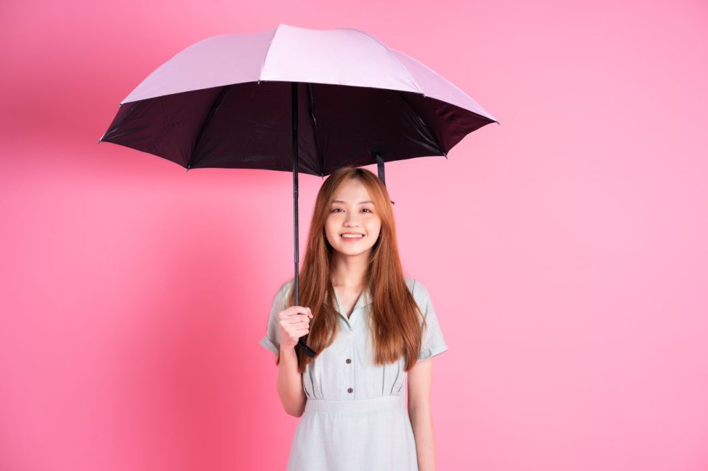 Smiling Asian teen girl holding pink umbrella against pink background