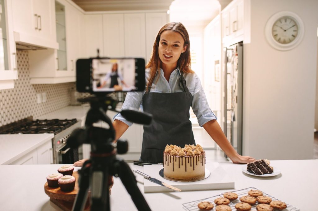 Woman stands in front of smartphone camera showcasing desserts.