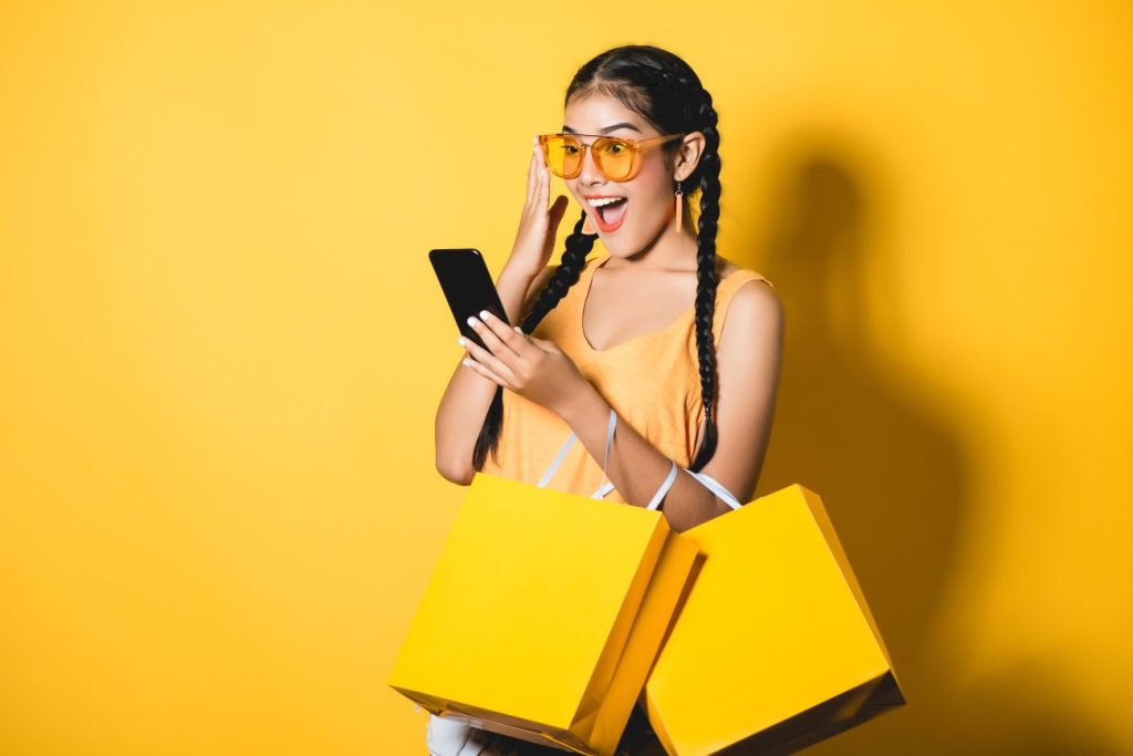 Teen girl against yellow background carrying yellow shopping bags