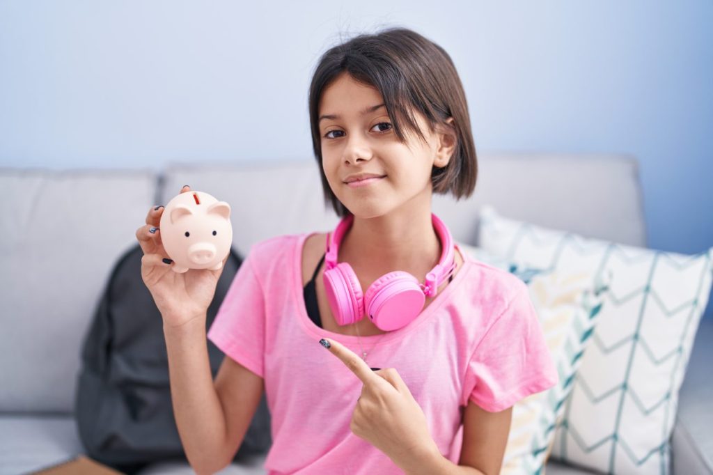 Young teen girl with pink tshirt and pink headphones holding pink piggy bank